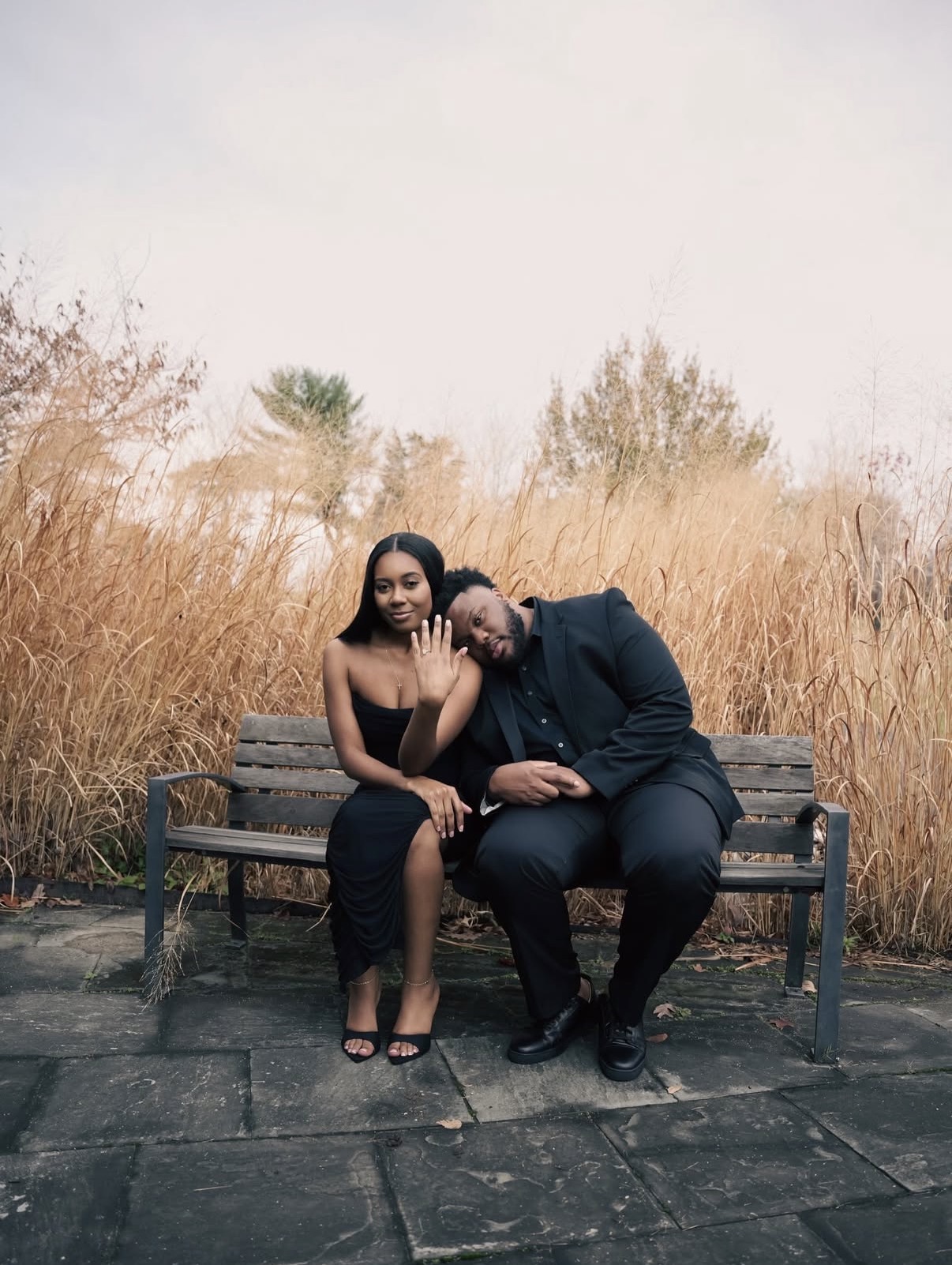 Engaged couple showing off the ring on a bench